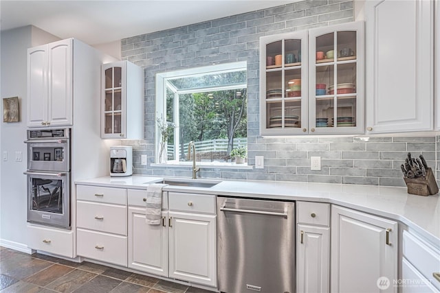 kitchen featuring stainless steel appliances, a sink, backsplash, glass insert cabinets, and white cabinetry