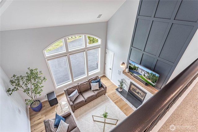 living room with a glass covered fireplace, high vaulted ceiling, light wood-style flooring, and baseboards
