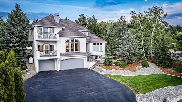 view of front of home featuring a balcony, stucco siding, an attached garage, asphalt driveway, and a chimney