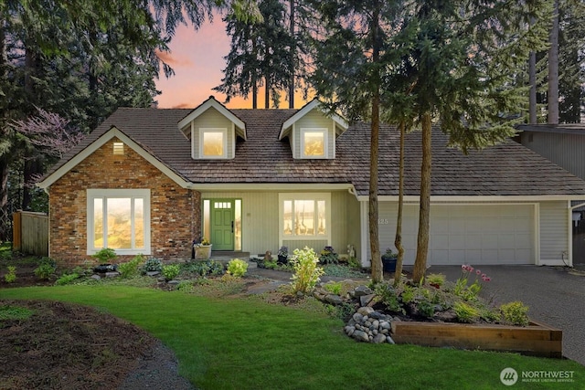cape cod house featuring a front lawn, an attached garage, driveway, and brick siding
