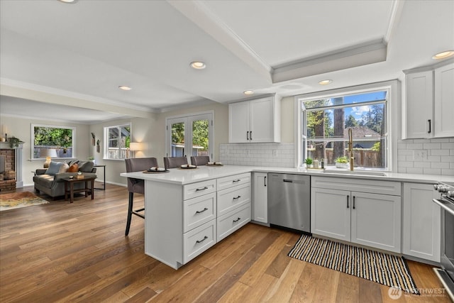 kitchen with stainless steel dishwasher, crown molding, a sink, open floor plan, and a peninsula