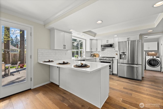 kitchen featuring stainless steel appliances, crown molding, a peninsula, plenty of natural light, and hardwood / wood-style flooring