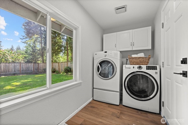 washroom featuring cabinet space, washing machine and clothes dryer, healthy amount of natural light, and dark wood-style flooring