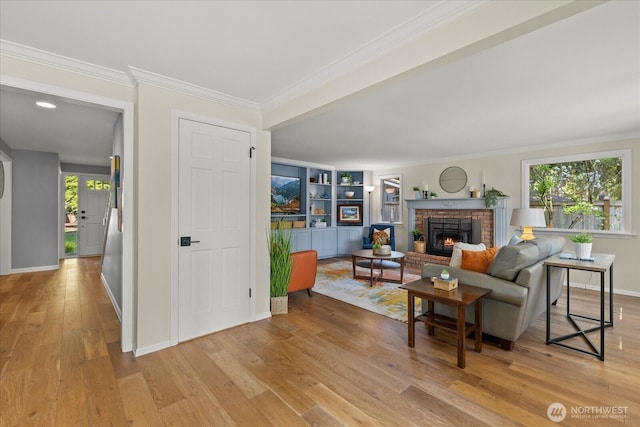 living room featuring light wood finished floors, crown molding, a brick fireplace, and baseboards