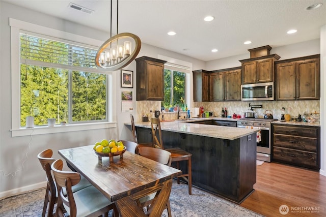 kitchen featuring visible vents, dark brown cabinets, light stone countertops, backsplash, and stainless steel appliances