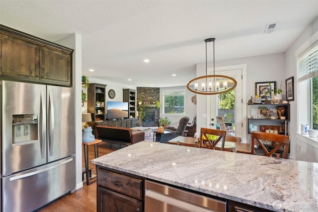 kitchen with light stone counters, wood finished floors, dark brown cabinets, and stainless steel fridge with ice dispenser