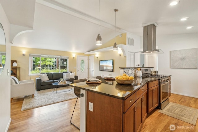 13503 Densmore Ave N, Seattle, WA 98133 - kitchen with stainless steel gas stove, island exhaust hood, brown cabinetry, a kitchen breakfast bar, and light wood finished floors