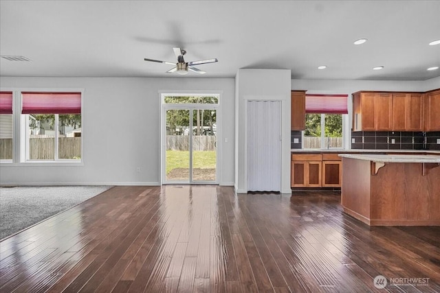 kitchen with a kitchen bar, ceiling fan, light countertops, open floor plan, and brown cabinetry