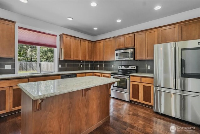 kitchen with stainless steel appliances, a sink, dark wood-type flooring, brown cabinetry, and recessed lighting