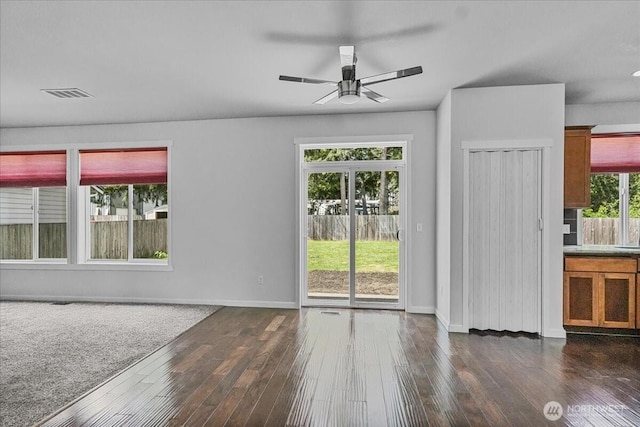 unfurnished living room with dark wood-type flooring, a ceiling fan, and baseboards