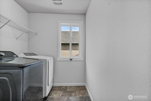 laundry area featuring washer and dryer, baseboards, and dark stone finish floors
