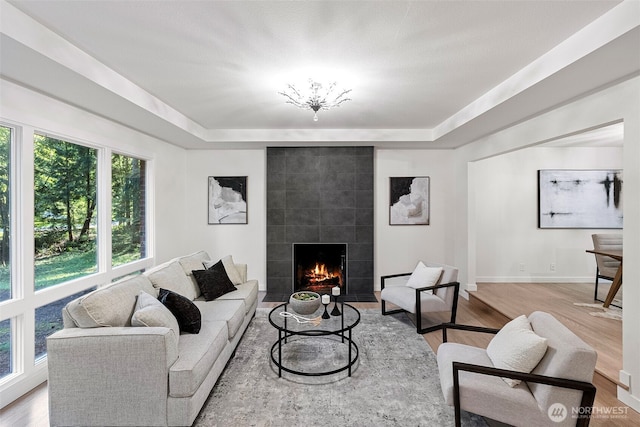 living area with baseboards, light wood-style floors, a tiled fireplace, and a tray ceiling
