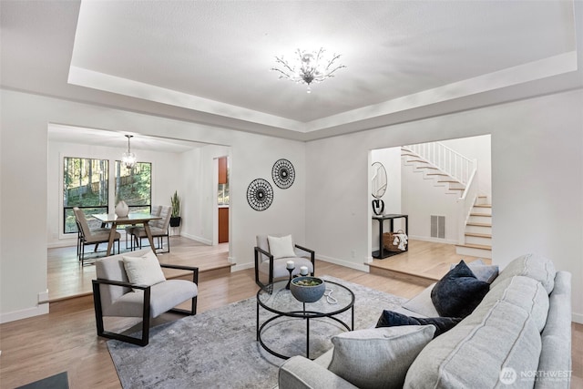 living room with a tray ceiling, a chandelier, baseboards, and stairway