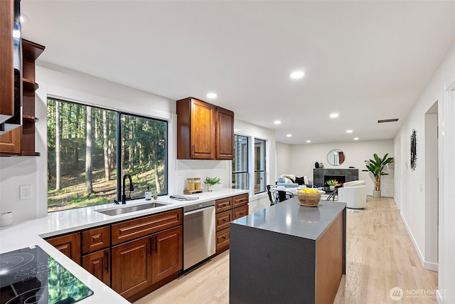 kitchen featuring light wood-style flooring, recessed lighting, dishwasher, a sink, and a tile fireplace