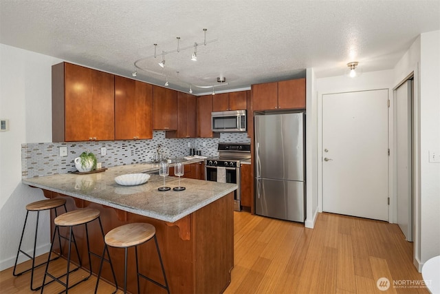 1751 NW 58th St Unit 4, Seattle, WA 98107 - kitchen with light wood-style floors, a peninsula, decorative backsplash, and appliances with stainless steel finishes