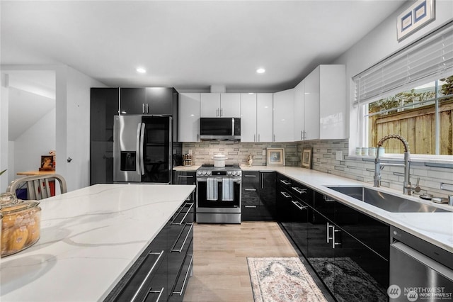 kitchen with appliances with stainless steel finishes, a sink, white cabinets, light wood finished floors, and dark cabinets