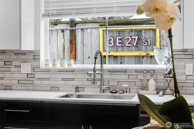 interior details featuring a sink, white cabinetry, light stone countertops, and tasteful backsplash