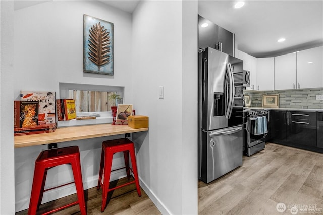 kitchen featuring a kitchen breakfast bar, appliances with stainless steel finishes, tasteful backsplash, light wood-type flooring, and recessed lighting