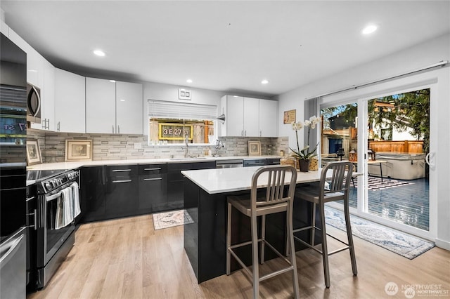 kitchen with decorative backsplash, light countertops, white cabinets, light wood finished floors, and stainless steel appliances
