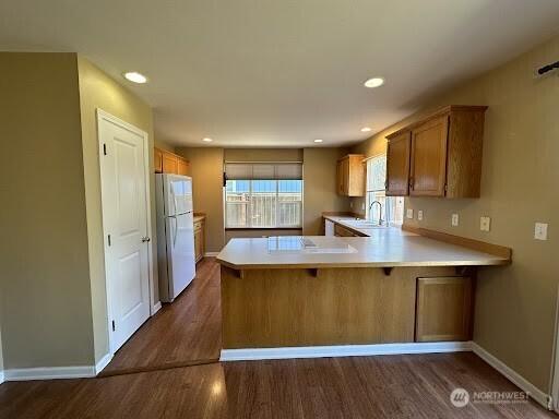 kitchen with freestanding refrigerator, a peninsula, light countertops, and dark wood-type flooring