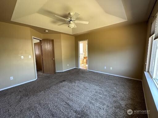 unfurnished room with a raised ceiling, ceiling fan, baseboards, and carpet floors