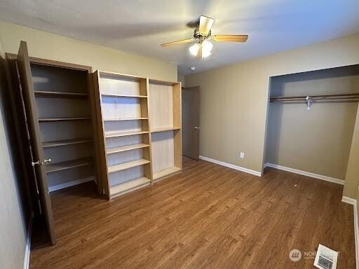 unfurnished bedroom with visible vents, baseboards, wood finished floors, and two closets