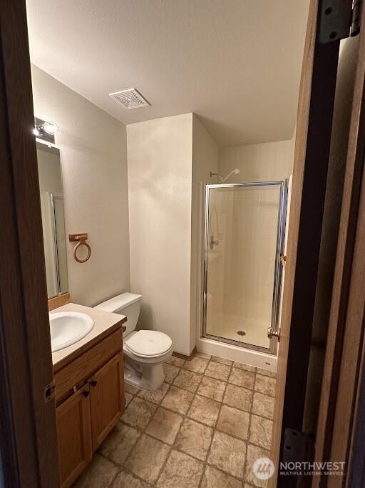full bathroom with stone finish floor, visible vents, a stall shower, vanity, and toilet