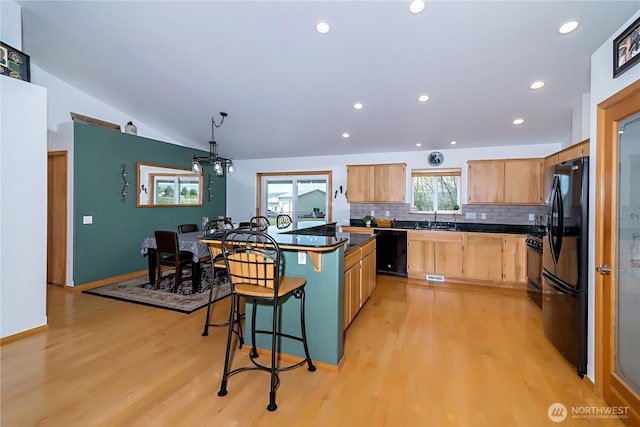 kitchen featuring light wood-style floors, dark countertops, a breakfast bar, and black appliances