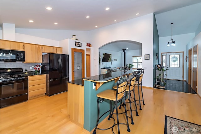 kitchen featuring a breakfast bar, light wood-style flooring, backsplash, black appliances, and vaulted ceiling