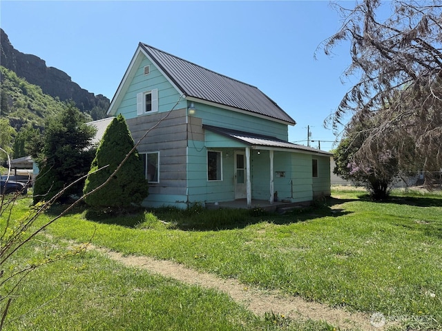 rear view of property with covered porch, a mountain view, a yard, and metal roof