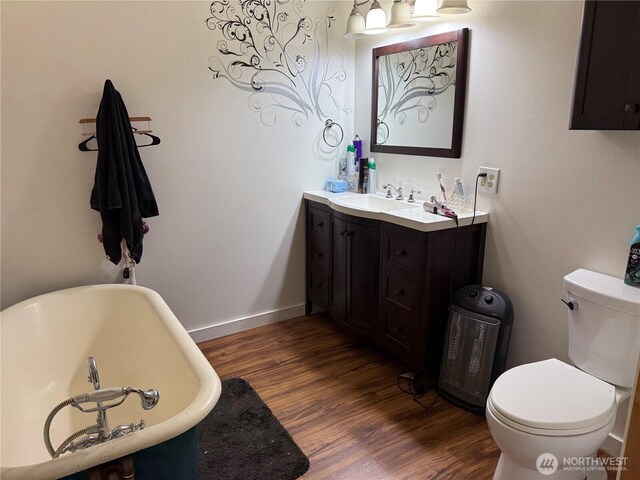 full bath with wood finished floors, vanity, baseboards, toilet, and a soaking tub