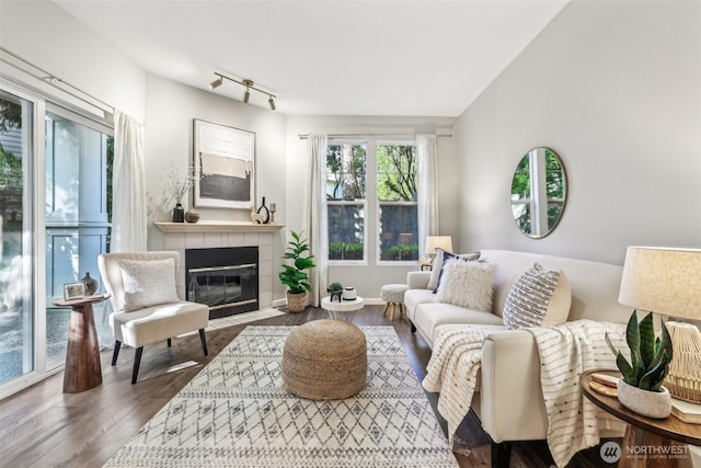 living room with a tiled fireplace, track lighting, and wood finished floors