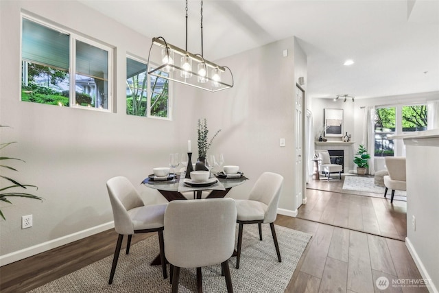 dining space with a tiled fireplace, baseboards, wood finished floors, and a notable chandelier