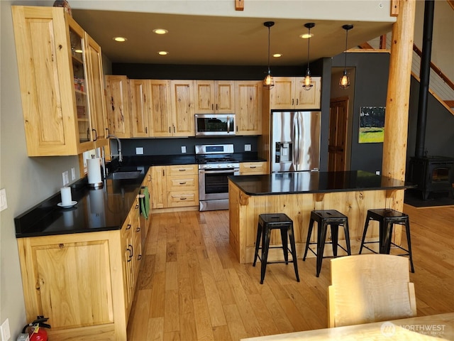 kitchen featuring light brown cabinetry, appliances with stainless steel finishes, dark countertops, and a sink