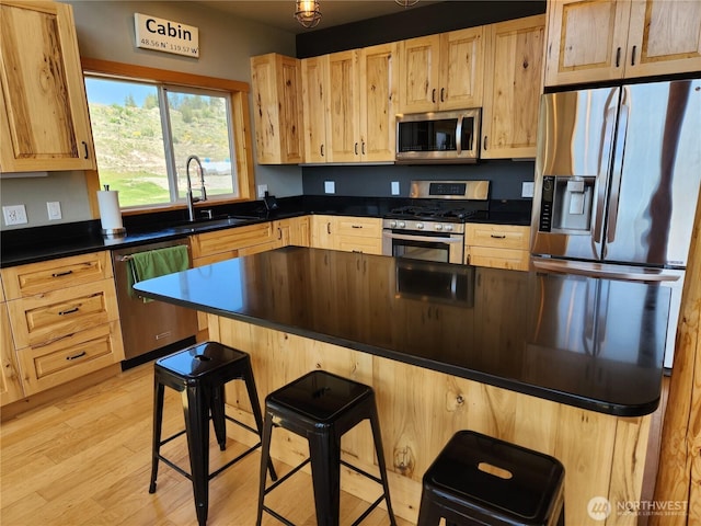 kitchen featuring a kitchen breakfast bar, light brown cabinetry, dark countertops, a sink, and stainless steel appliances