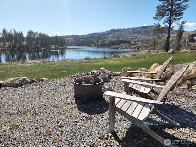 exterior space with a water view, a view of trees, and a fire pit