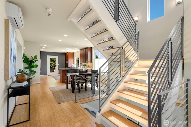 stairs with recessed lighting, plenty of natural light, wood finished floors, and a wall mounted air conditioner