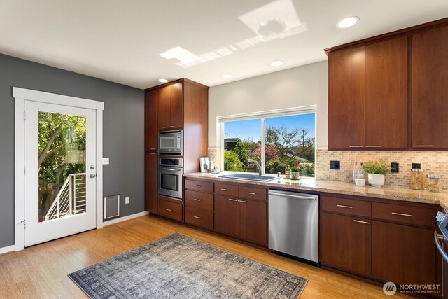 kitchen featuring a sink, light wood-style floors, stainless steel appliances, a wealth of natural light, and tasteful backsplash