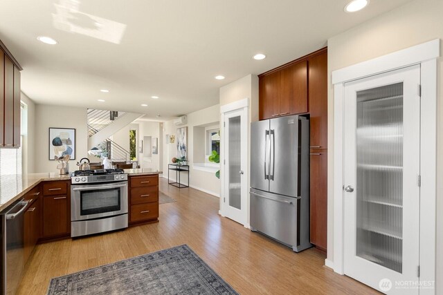 kitchen featuring a peninsula, recessed lighting, light stone counters, light wood-style flooring, and stainless steel appliances
