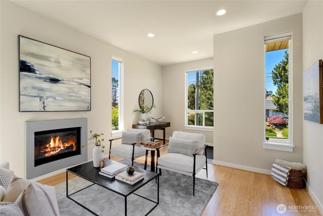living area featuring a glass covered fireplace, baseboards, recessed lighting, and light wood-style flooring