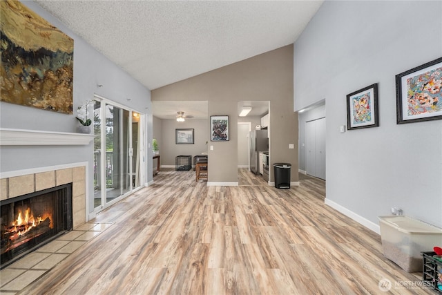unfurnished living room with wood finished floors, a fireplace, a textured ceiling, high vaulted ceiling, and baseboards