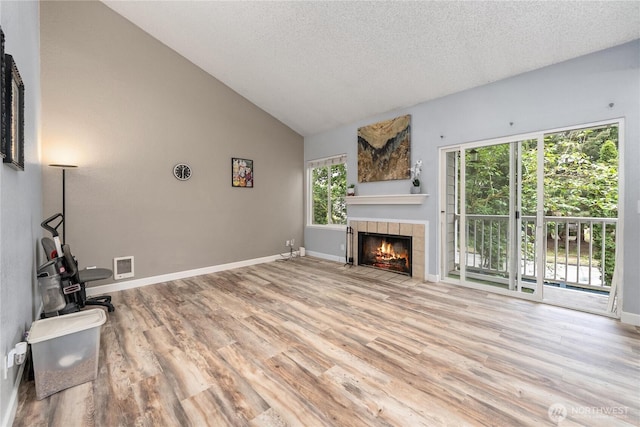unfurnished living room featuring wood finished floors, a fireplace, a textured ceiling, baseboards, and high vaulted ceiling