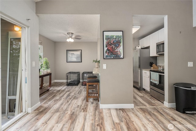 kitchen with stainless steel appliances, light wood finished floors, white cabinets, a ceiling fan, and baseboards