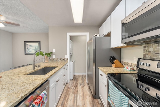 kitchen featuring stainless steel appliances, a sink, stacked washer / drying machine, light wood finished floors, and white cabinets