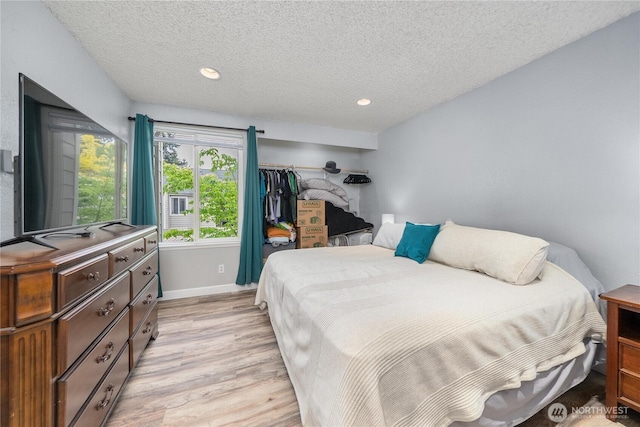 bedroom with light wood-style floors, a textured ceiling, baseboards, and recessed lighting