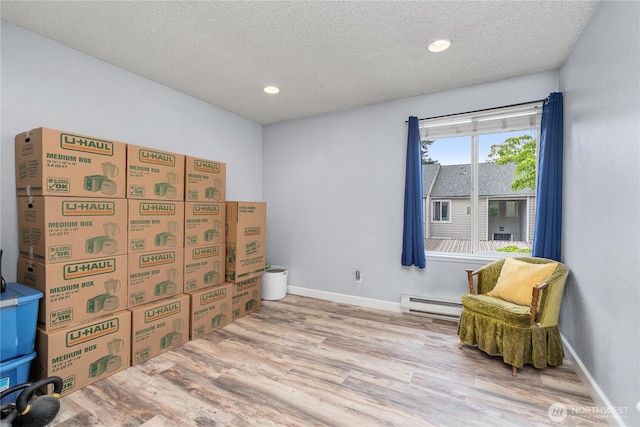 living area with baseboard heating, a textured ceiling, wood finished floors, baseboards, and recessed lighting