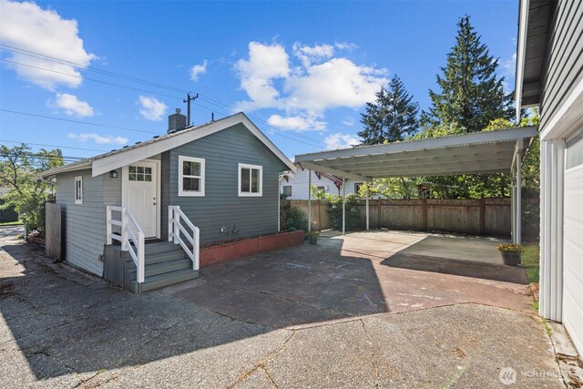 view of front of house featuring driveway, fence, a detached carport, a patio, and central air condition unit