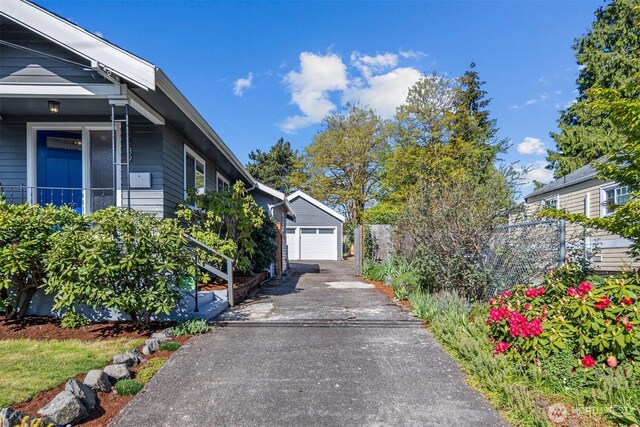 view of property exterior with asphalt driveway, a detached garage, an outbuilding, and fence