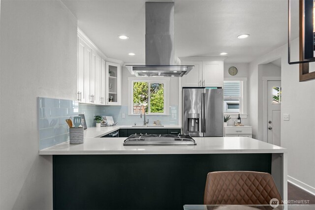 kitchen with appliances with stainless steel finishes, island exhaust hood, a sink, decorative backsplash, and light countertops