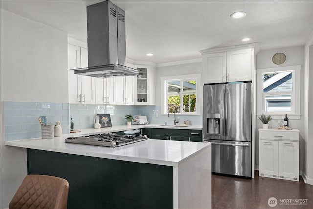 kitchen featuring appliances with stainless steel finishes, island range hood, a sink, a peninsula, and light countertops